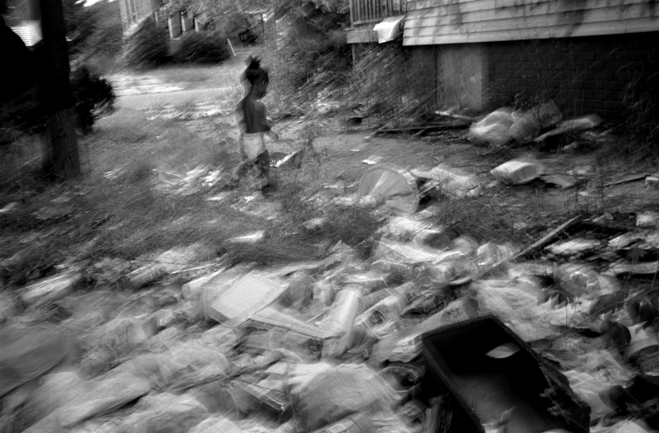 A child runs through garbage in the driveway of the abandoned house adjacent to his home. 