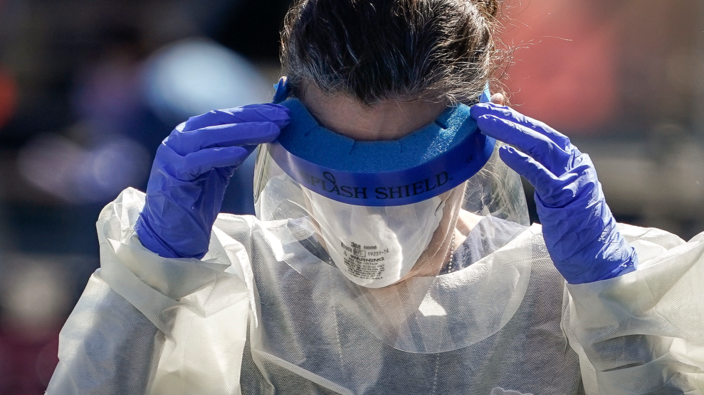 A worker in an N-95 mask, gloves, cover-alls, and a face shield on their eyes.