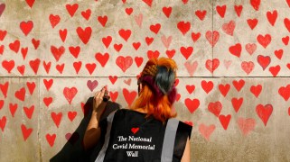 A woman draws red hearts representing individual coronavirus deaths onto the newly-unveiled National Covid Memorial Wall opposite the Houses of Parliament in London, England, on March 30, 2021.
