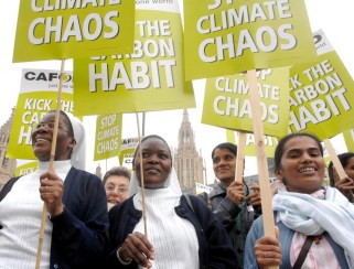 Group of climate protesters crowded together hold signs. 