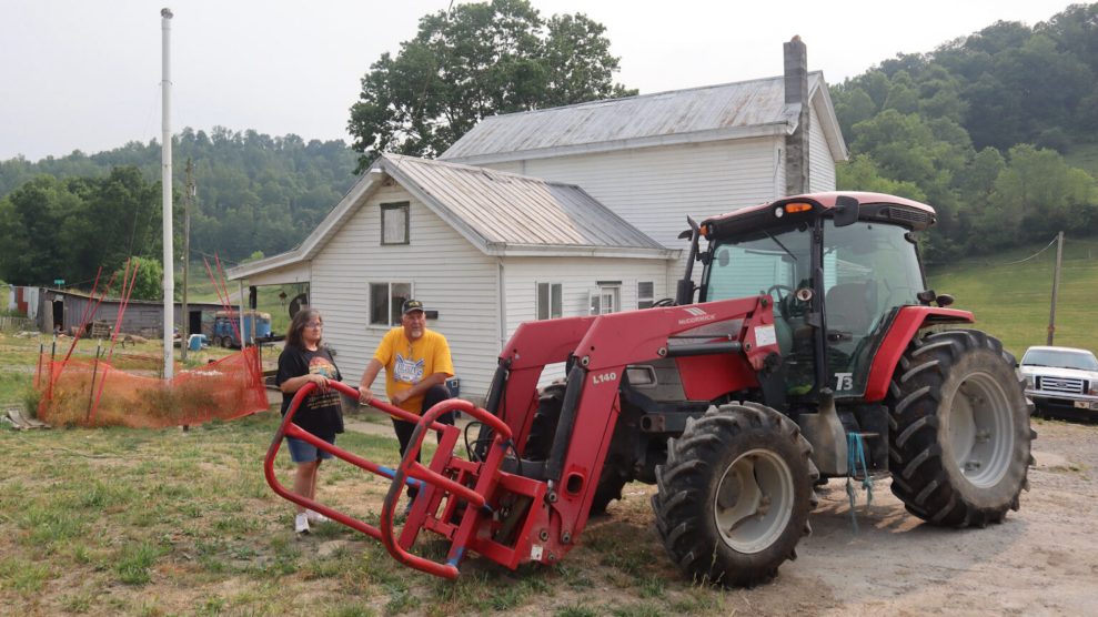 Two white middle-aged people, Melissa and Jim Nestor, outside a white building with a red tractor