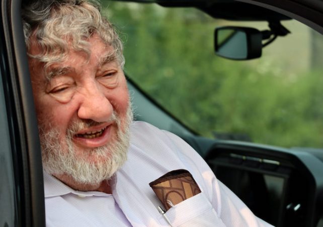 Jack Spadero, a white man with white hair, sits in a car and is wearing a light pink shirt