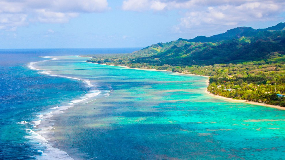 A photo of the area of where Rarotonga, the largest of Cooks' Islands, meets the ocean. The sky is blue.