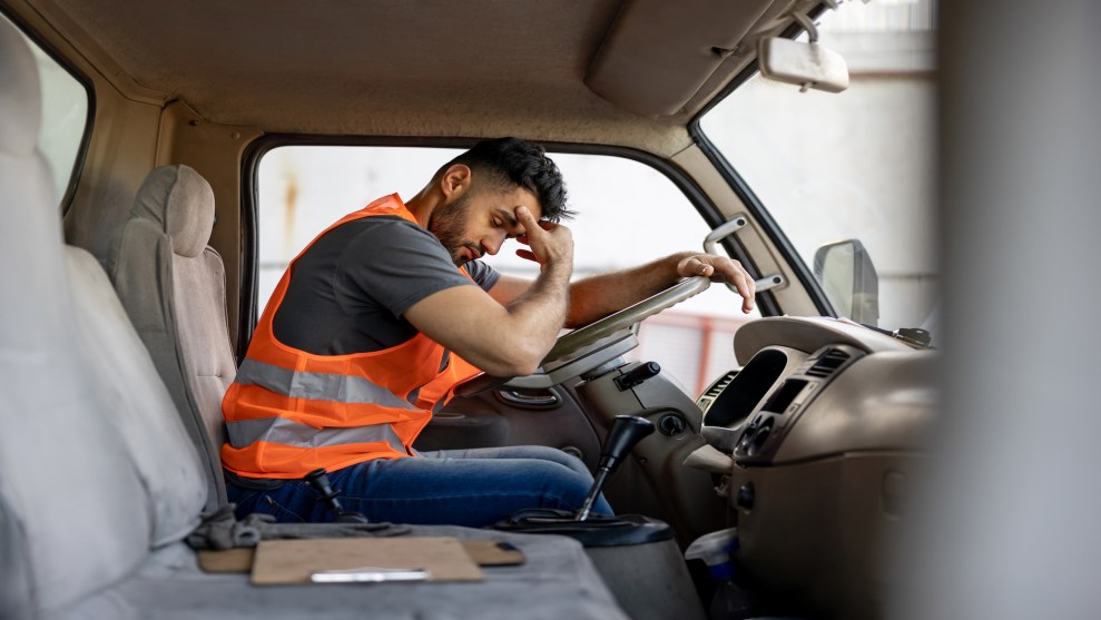 Truck driver in orange vest puts head in hand.