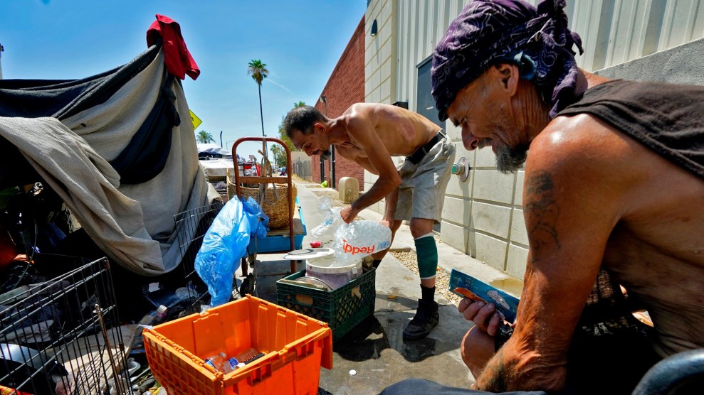 Two white shirtless men crouch near a tent made of tarps. One fills a jug with water and ice. The sky is a gradient of deep blue to white.