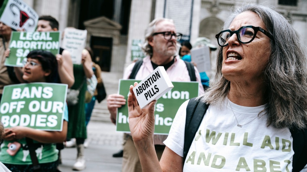 A protester wears a shirt that says "I will aid and abet abortion" while holding up a box labeled "abortion pills."