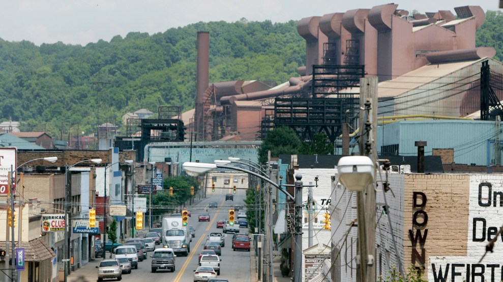 A large, brick chemical plant sits behind a city road, filled with cars.