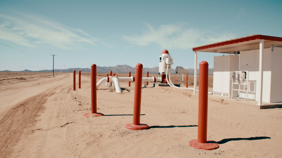 A new groundwater pump that is red and white, in the middle of a desert area.