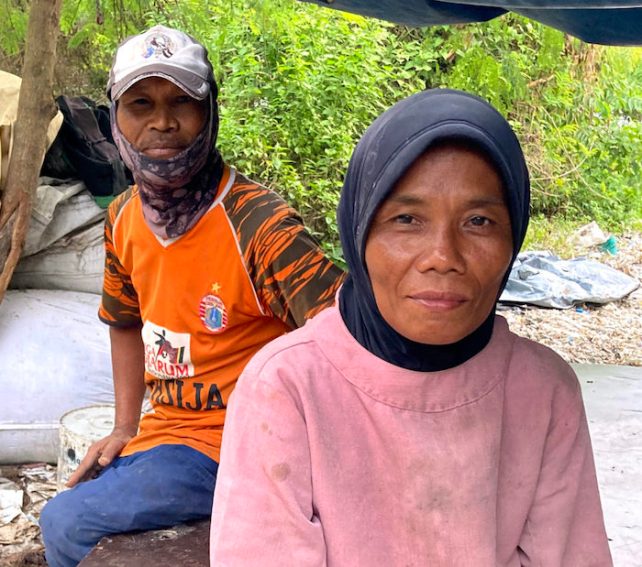 Kasih, who has brown skin and is wearing a black head covering and pink top, next to her husband, wiho has dark brown skin, wearing a cap, orange shirt and jeans.