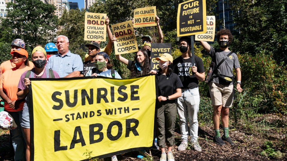 A group of people, mostly masked, hold yellow and black signs with slogans like "Our future is non negotiable" and "Pass a bold civilian climate corps." In front of them several hold a banner that says "Sunrise stands with labor."