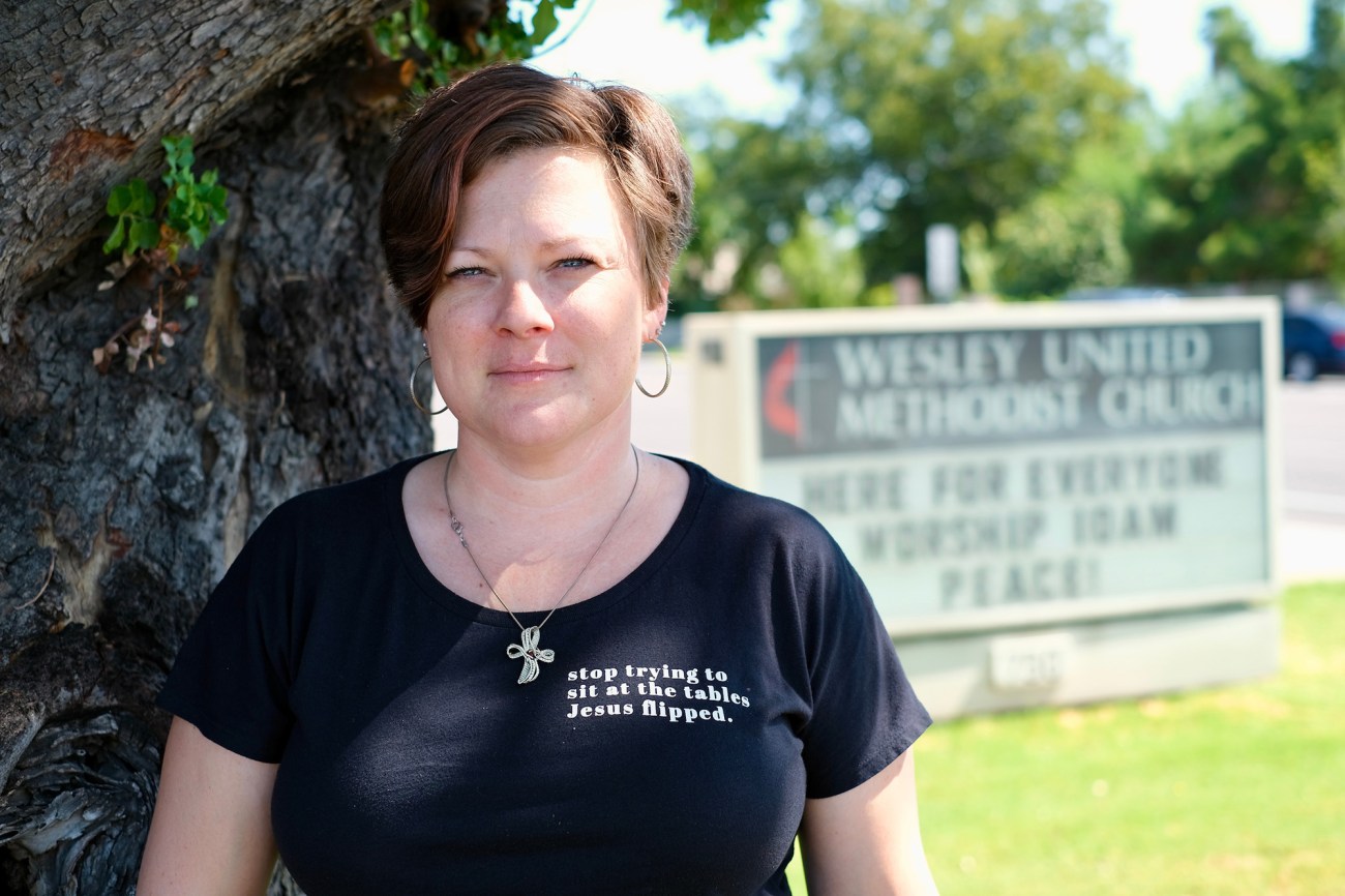 Woman pastor standing by a tree with a church sign in the background.