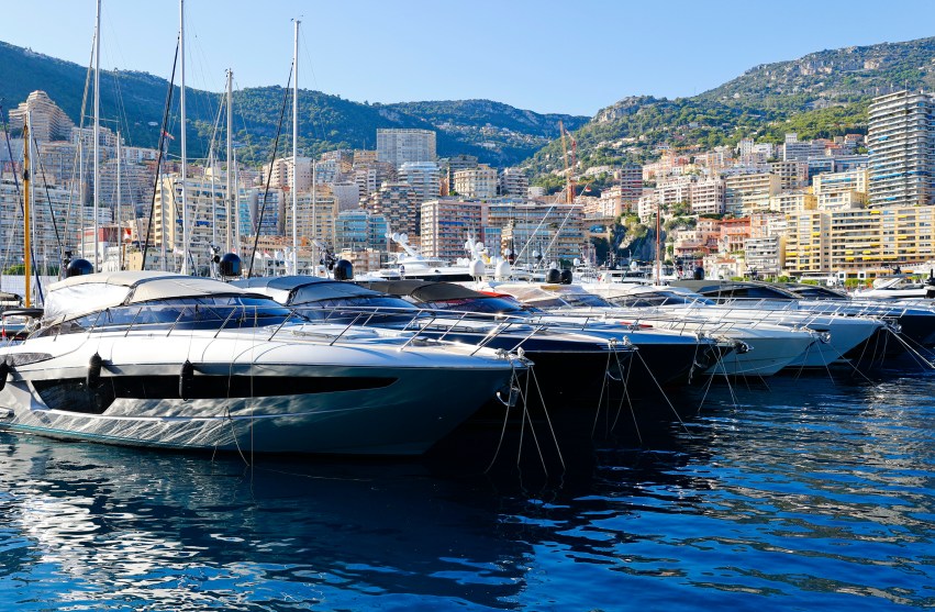 A tight shot of some clearly expensive boats at the Monaco Yacht show in Monte Carlo, September 27, 2023, from the water side, with shoreline buildings and hills in the backdrop.