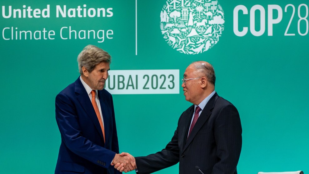 Two men shake hands in front of a wall that says "United Nations Climate Change Dubai 2023." The man on the left is a white American and taller, and the second man is slightly shorter and Chinese.