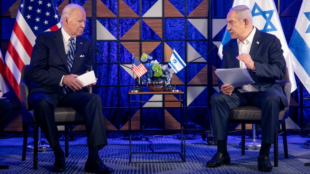 President Joe Biden listens to Prime Minister Benjamin Netanyahu. They are seated next to each other, each flanked by the flags of their respective nations.