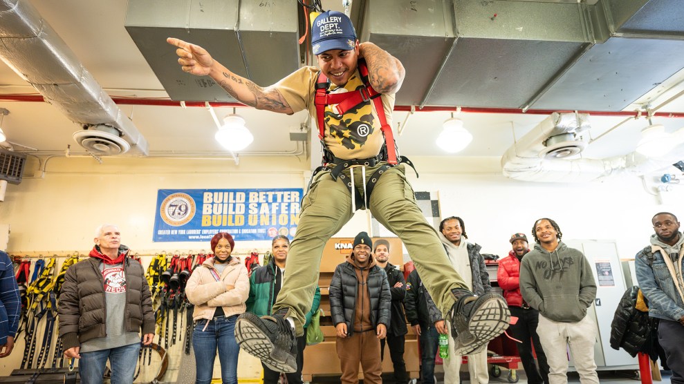 Smiling man hanging suspended in a harness in front of a classroom.