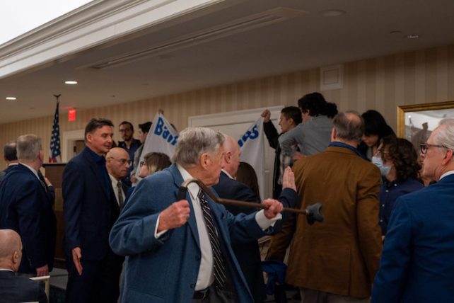 Some protestors holding up a sign in a room with a dinner, with people approaching the protestors, with one person holding up a cane pointed towards them