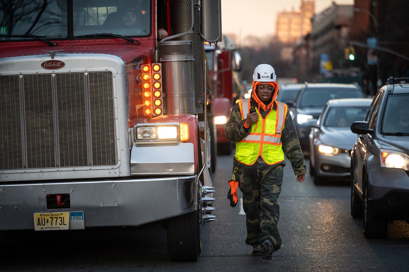 Woman in yellow vest walking next to a semi truck in traffic.