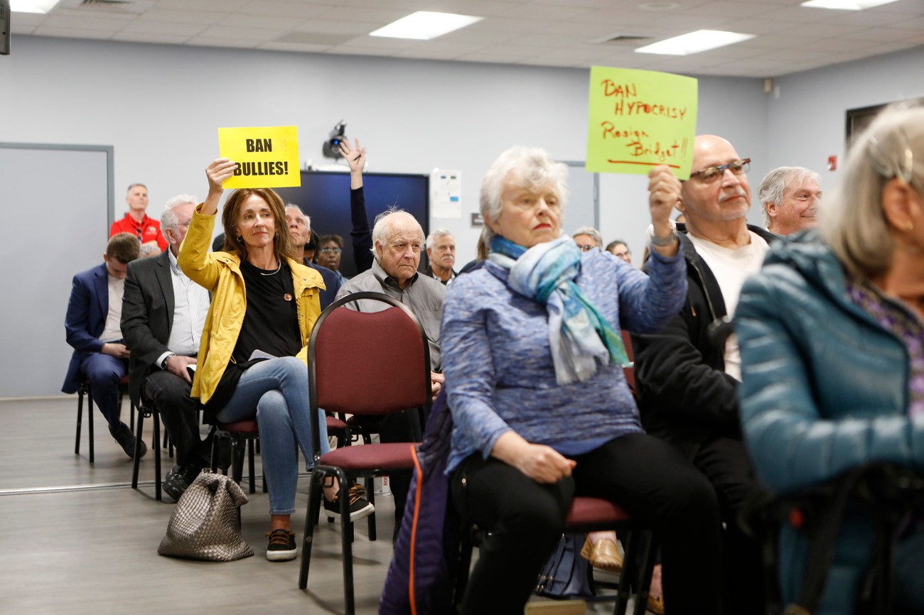 People sitting in a meeting holding up yellow protest signs.