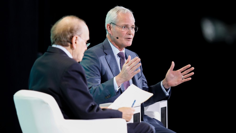 A white man sits with his hands spread open, mid speech. Another man, not facing the camera, sits next to him.