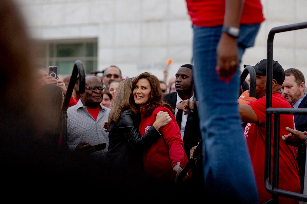 Photo of Michigan Governor Gretchen Whitmere being hugged, smiling as she waits to go on a stage to speak.