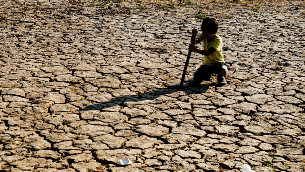 A boy bends over ground that is so dry cracks break through it.