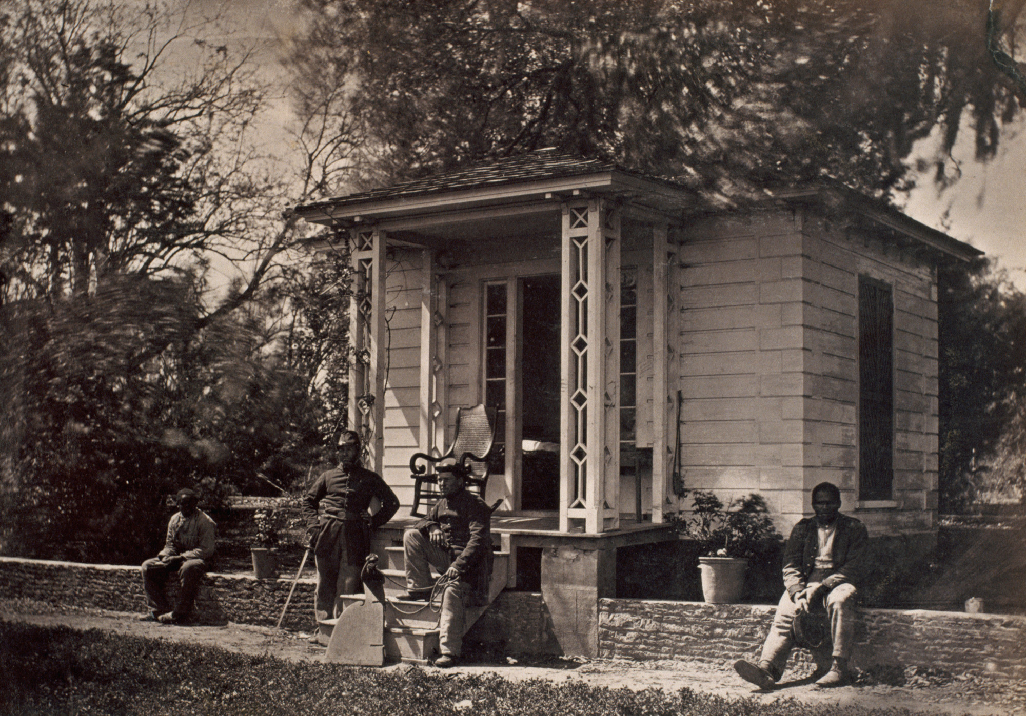 Black-and-white photo of four men sitting in front of a small building.