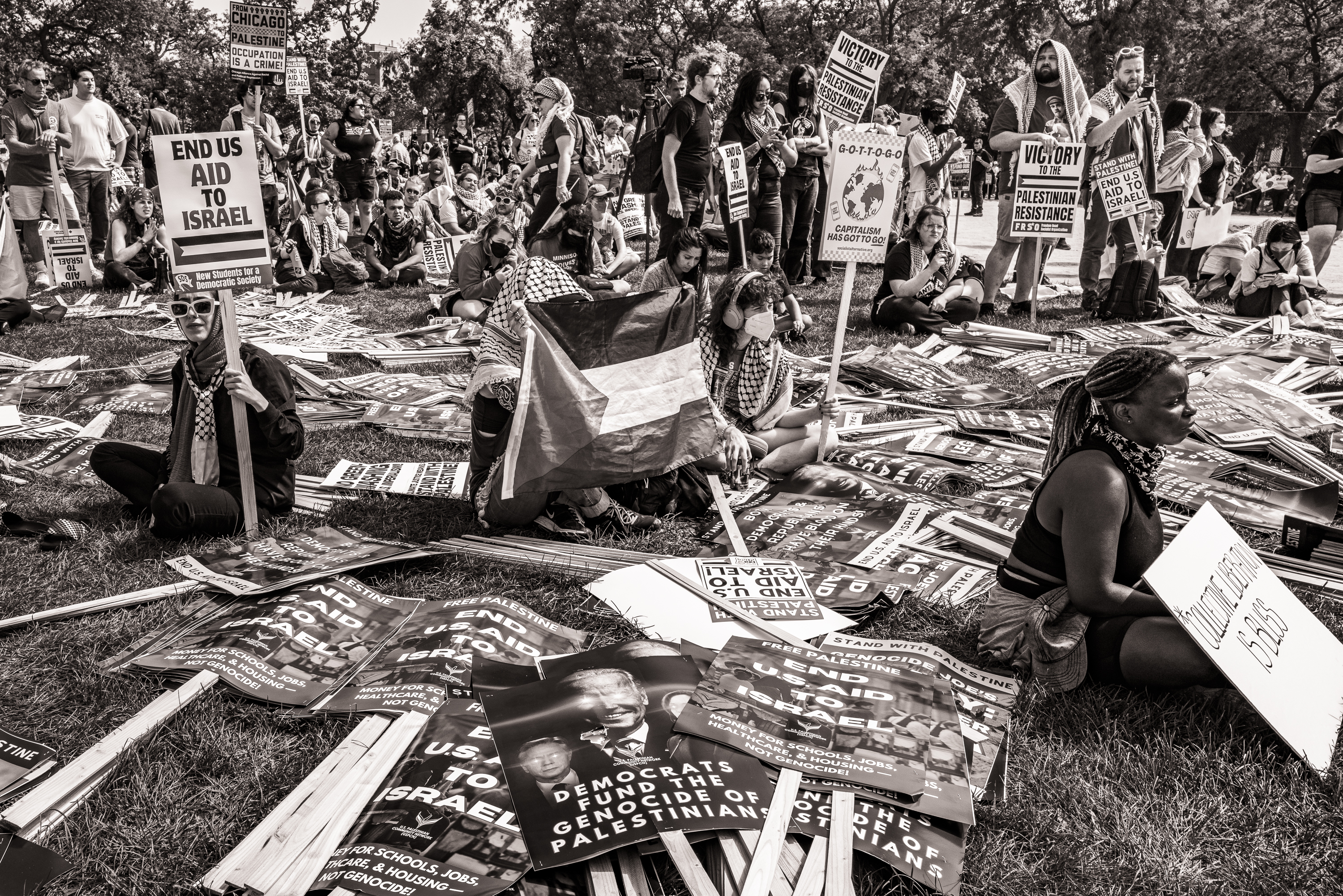 Black and white photo of a group of protesters gathering around scattered signs laying on the ground.