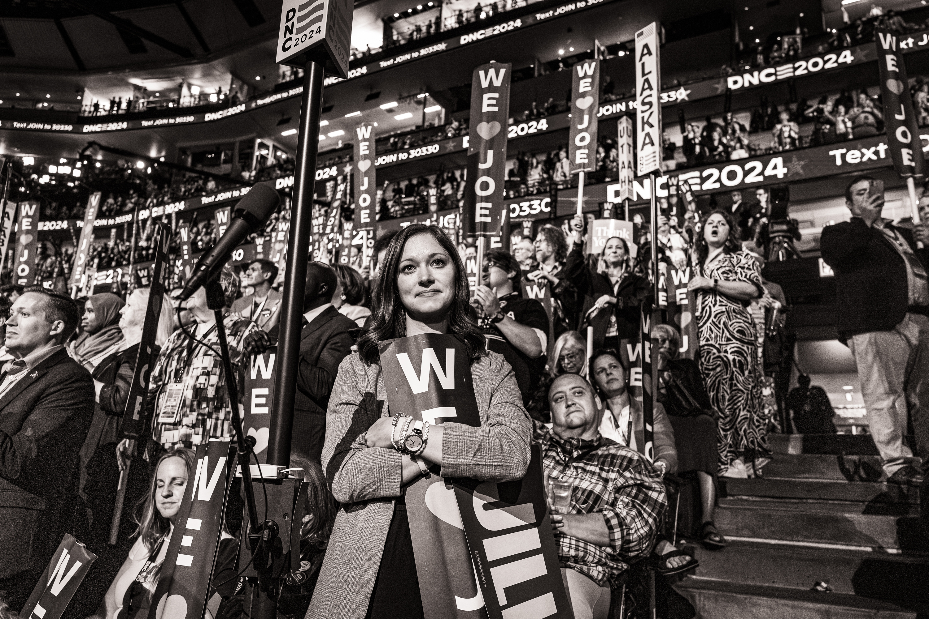 Black and white photo of a woman among a large crowd, holding a We Love Joe sign close to her chest