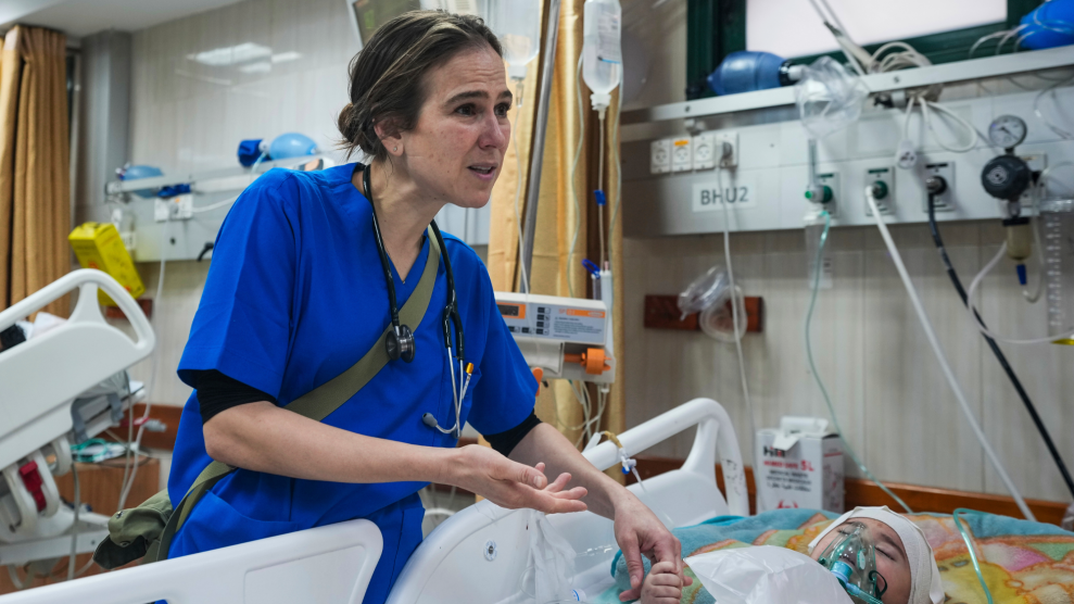 Dr. Tanya Haj-Hassan, in blue scrubs, holds the fingers of an injured child lying in a hospital bed.