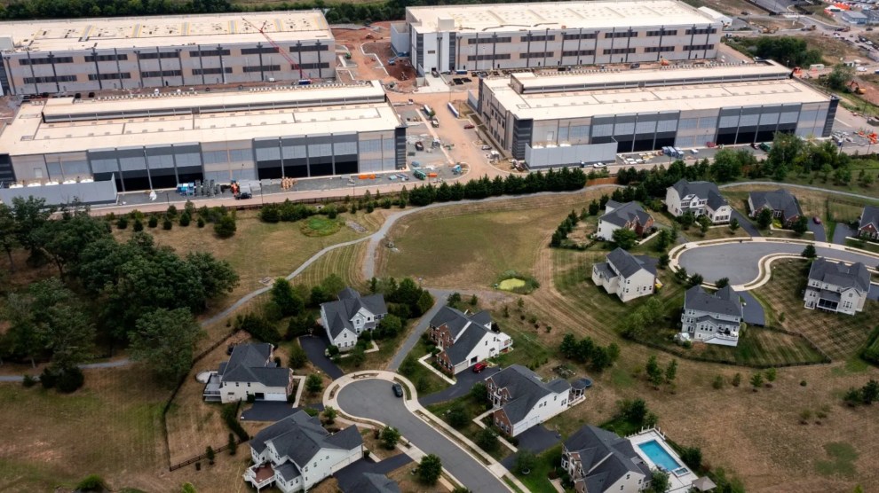 A giant data center consisting of four white blocky buildings abutting a piece of land with two residential cul-de-sacs with identical-looking white houses.