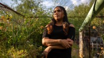 A woman in black with long hair stands in a garden plot.