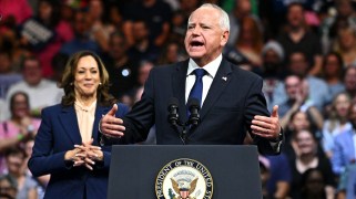 Tim Walz stands at a podium with the President of the US seal to give a rally speech with Kamala Harris