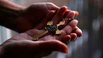 A woman's cupped hands hold a golden cross.