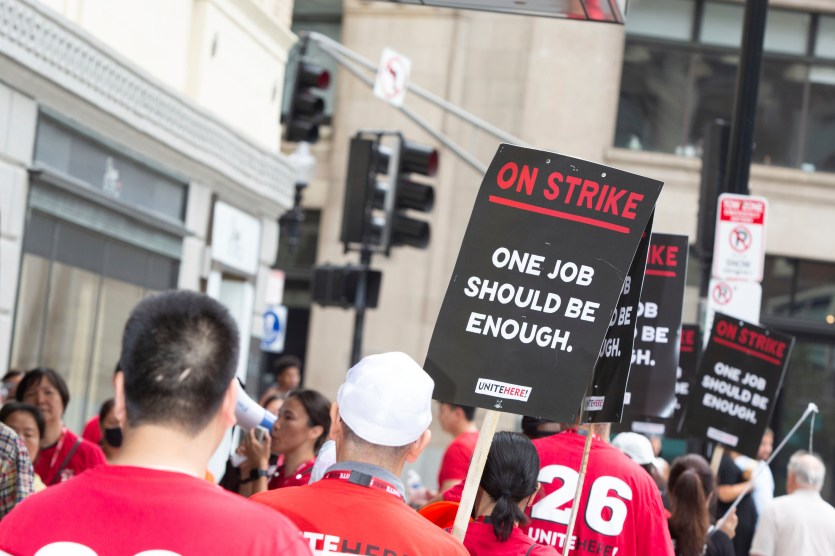 Workers in red shirts hold up black picket signs.