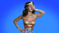 Wonder Woman, played by Lynda Carter, stands with one hand on her hip and one hand holding her head.