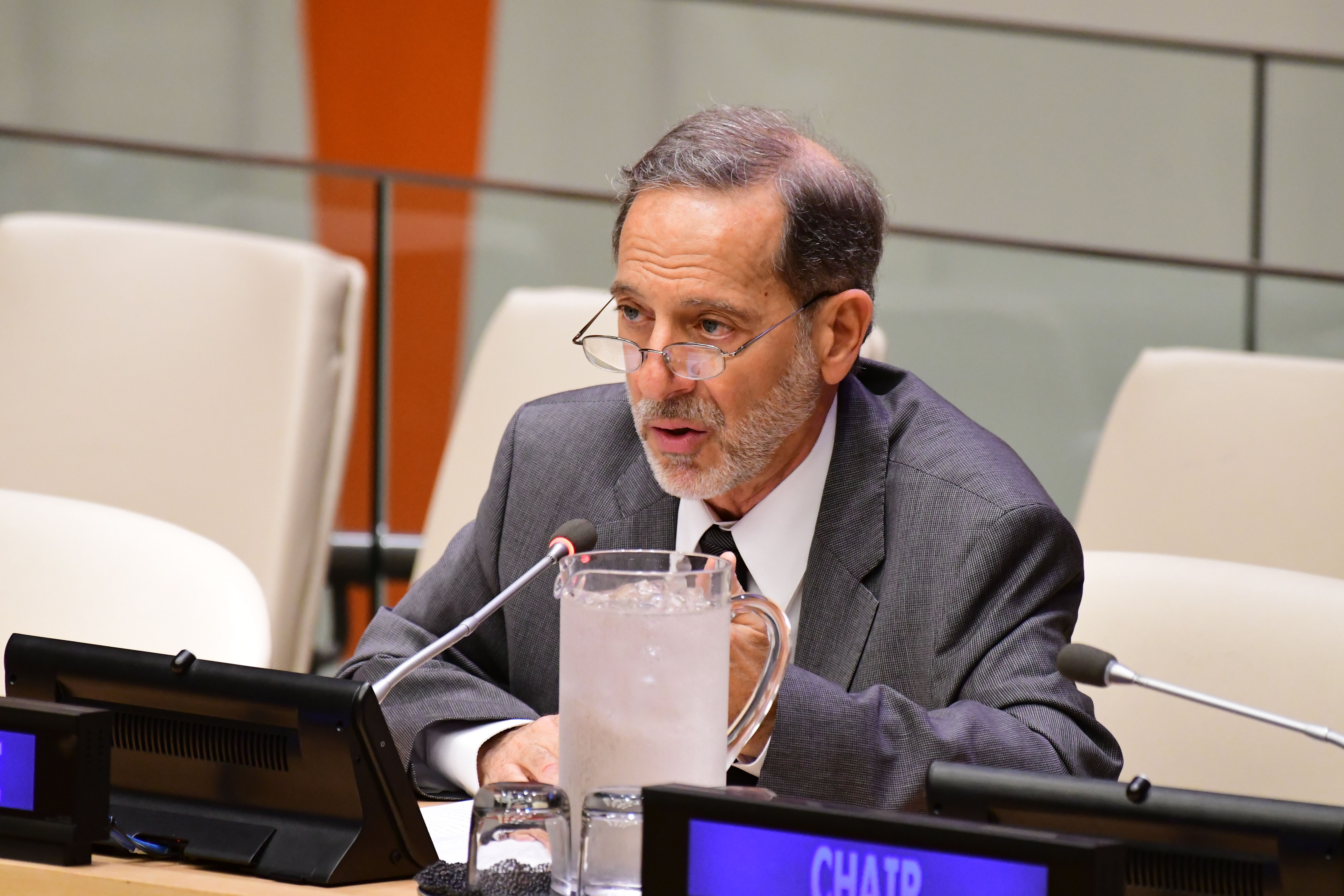 Professor Rashid Khalidi, dressed in a suit and tie, speaks into a microphone. 