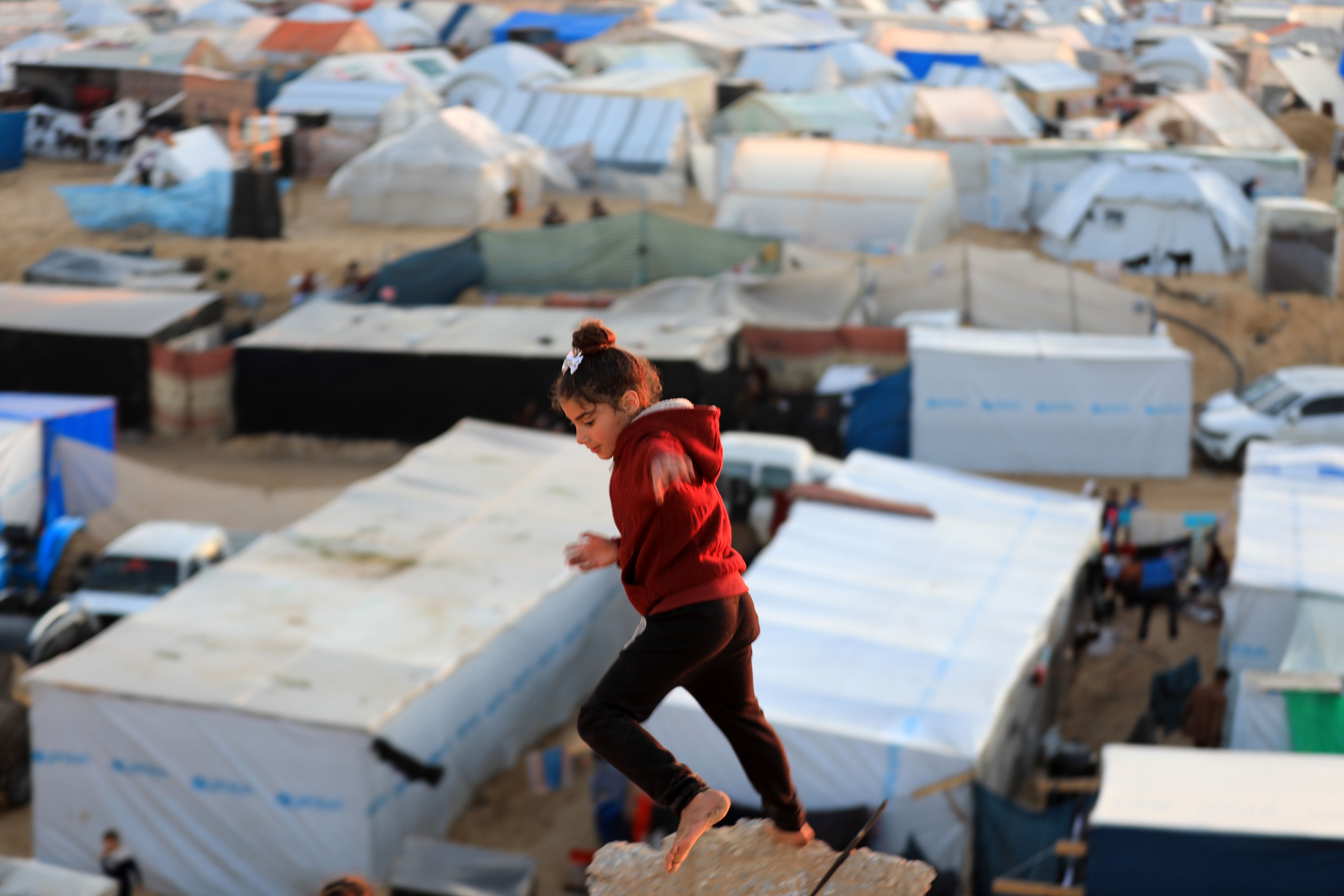 A barefoot girl runs above an encampment.