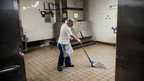 A man wearing a hairnet mops a tile floor.