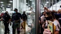 A crowd of Trump supporters and election challengers stand outside of a building with their phones raised; inside three policemen guard poll workers who are counting votes of the 2020 election.