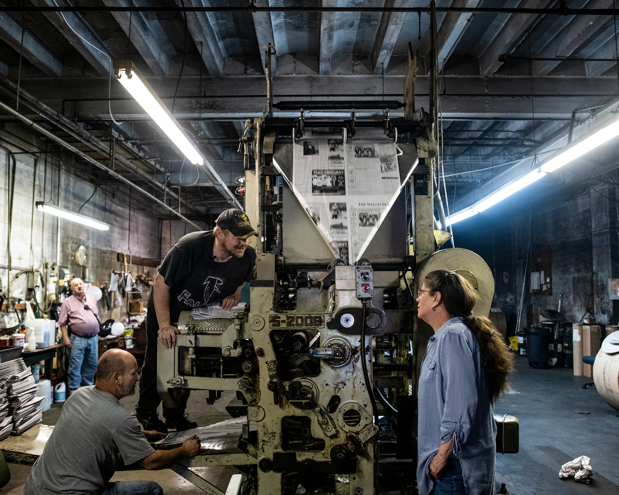 Three people stand around a large newspaper printing press.