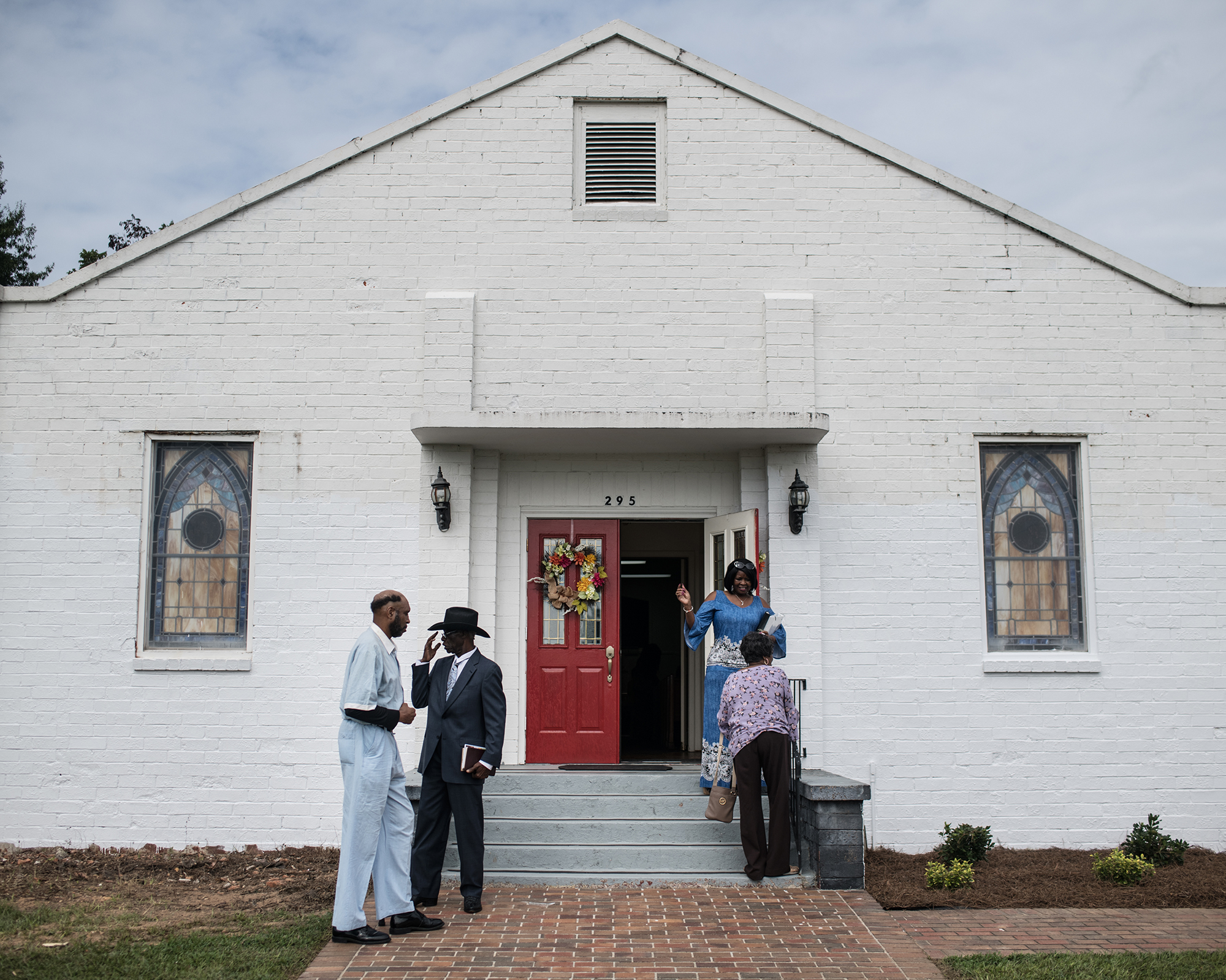 People standing outside a small white church with its door open.