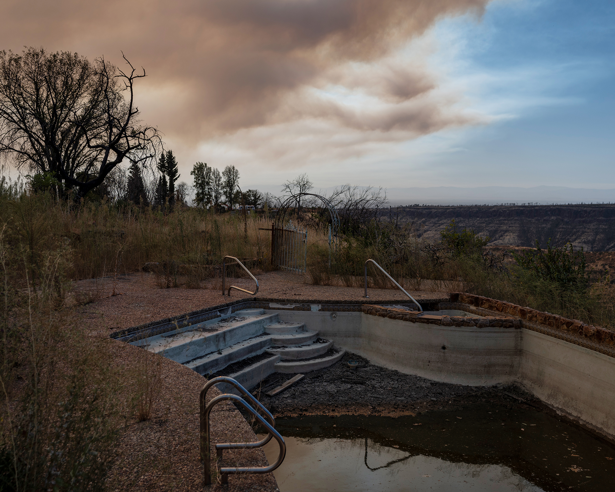 Empty swimming pool surrounded by land burned by fires.