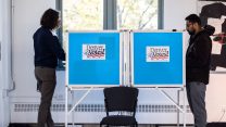 Two people stand at voting booths with signs that read, "Denver Votes!"