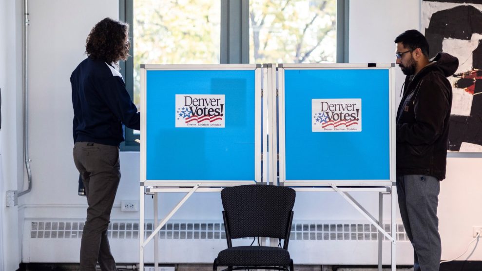 Two people stand at voting booths with signs that read, "Denver Votes!"