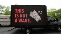 A message on a black truck that says, "This is not a wage" with a few dollars crumpled and a few coins.