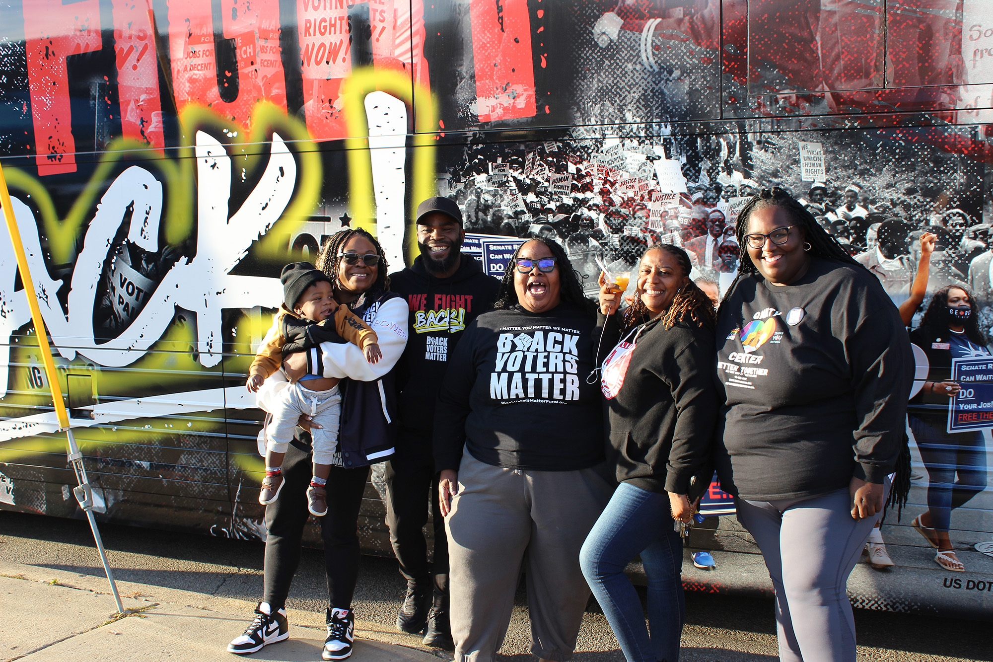 Five people and a baby pose in front of a mural.