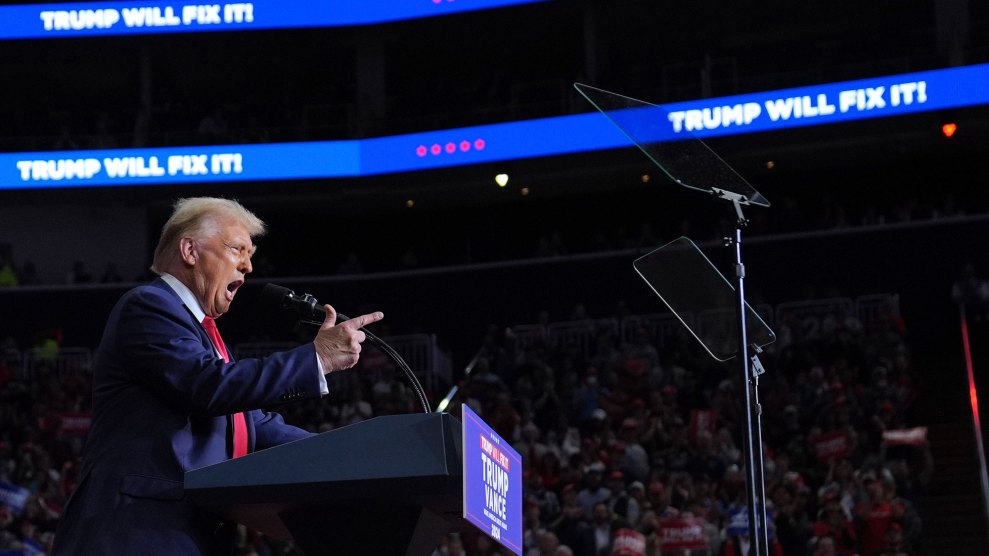 Donald Trump points his index finger at the crowd from behind his podium on a campaign stop, with his mouth open.