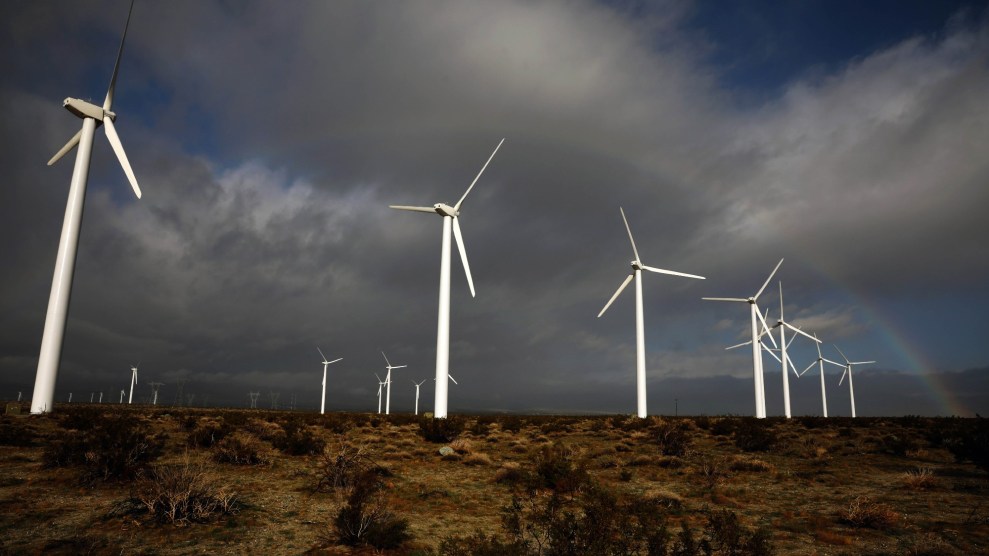 A rainbow rises up behind a wind farm of white turbines