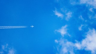 A plane flies overhead in a slightly cloud blue sky