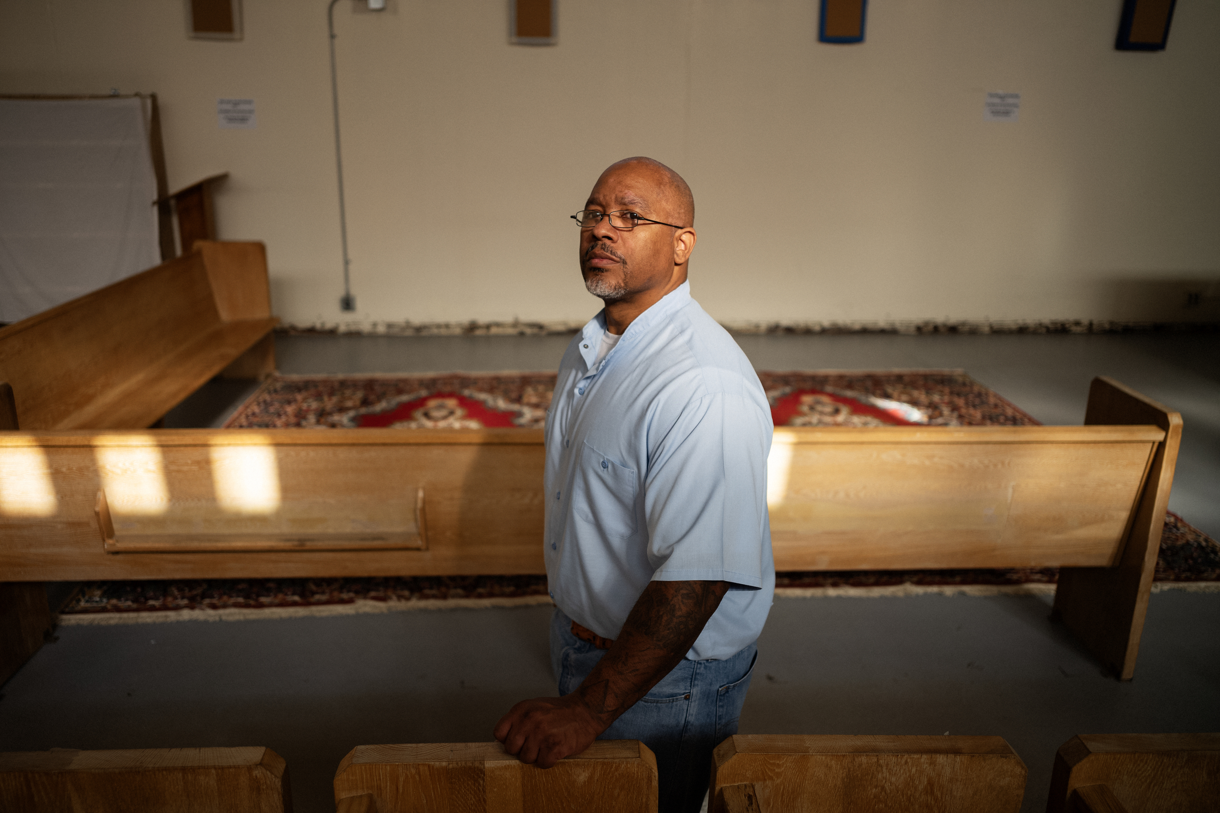 Man standing beside a pew in a chapel.